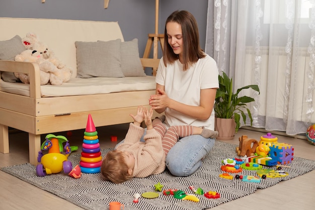 Indoor shot of young beautiful mother playing and having fun on the floor with her little daughter mom and kid clapping hands play games singing nursery rhymes and finger gymnastics