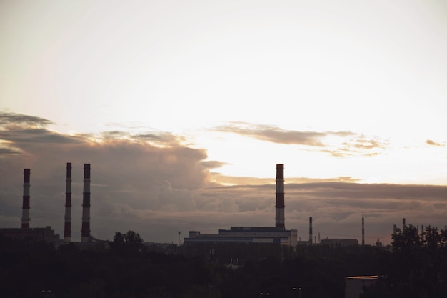 Industrial brick chimneys against textured sunset sky. Concept of production and environmental pollution in metropolis. City background textured banner. Copy space for site