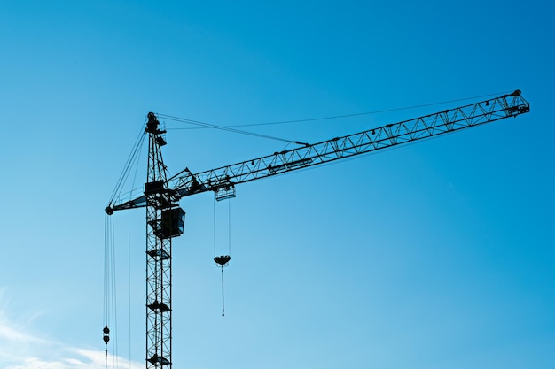 Industrial construction crane silhouette against blue sky building