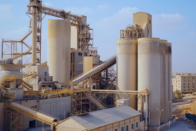 Photo industrial equipment processing cement in a factory setting with large silos and a network of conveyors