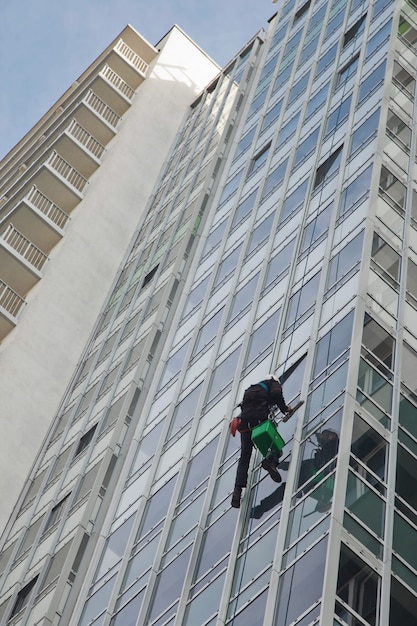 Photo industrial mountaineering worker hangs over residential building while washing exterior facade glazing. rope access laborer hangs on wall of house. concept of urban works. copy space