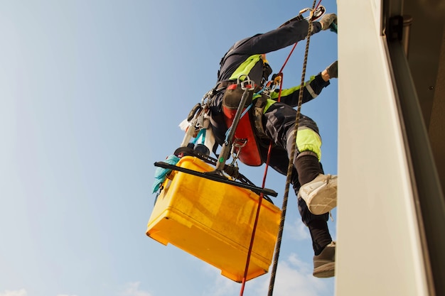 Industrial mountaineering worker hangs over residential building while washing exterior facade glazing. Rope access laborer hangs on wall of house