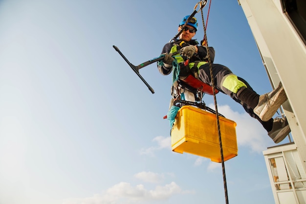 Industrial mountaineering worker hangs over residential building while washing exterior facade glazing. Rope access laborer hangs on wall of house