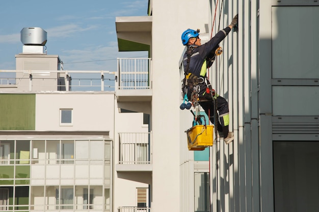 Industrial mountaineering worker hangs over residential building while washing exterior facade glazing