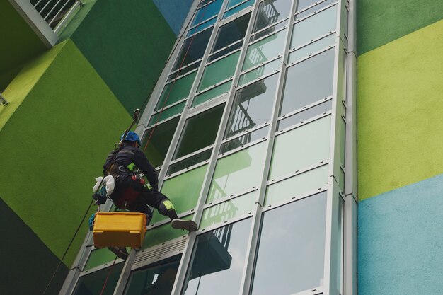 Photo industrial mountaineering worker hangs over residential facade building while washing exterior facade glazing. rope access laborer hangs on wall of house. concept of urban works. copy space for site