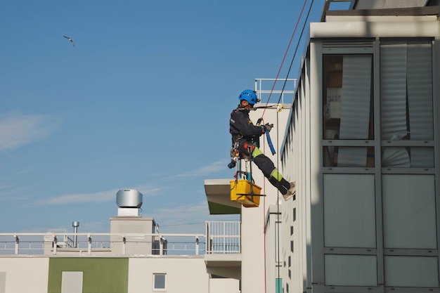 Industrial mountaineering worker hangs over residential facade building while washing exterior facade glazing. Rope access laborer hangs on wall of house. Concept of urban works. Copy space for site