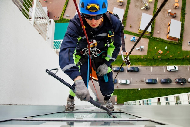 Photo industrial mountaineering worker hangs over residential facade building while washing exterior facade glazing. rope access laborer hangs on wall of house. concept of urban works. copy space for site