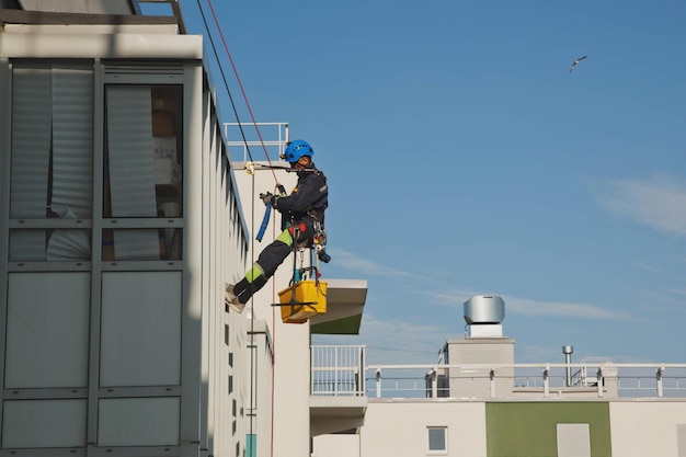 Industrial mountaineering worker hangs over residential facade building while washing exterior facade glazing