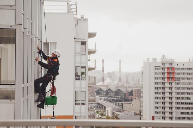 Industrial mountaineering worker hangs over residential facade building while washing exterior facade glazing