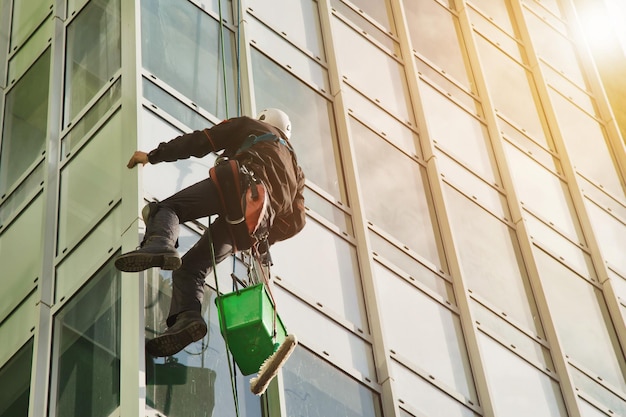 Industrial mountaineering worker in uniform washing exterior glazing over residential facade building