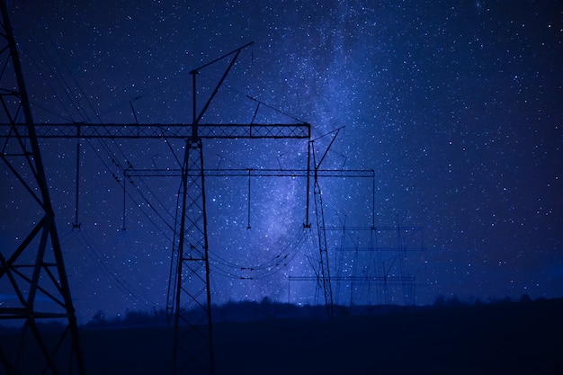 Industrial night landscape with high-voltage power line, electric tower and stars an sky