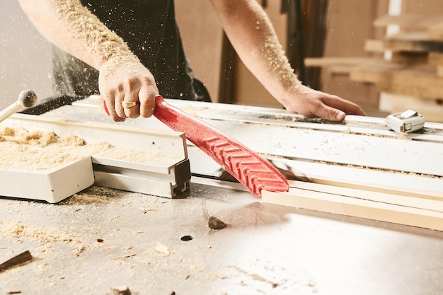 Industrial worker cuts wood on a woodworking machine closeup Manual cutting carpentry industry