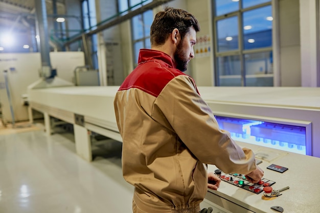 Industrial worker operating automated machine for wood processing in a factory