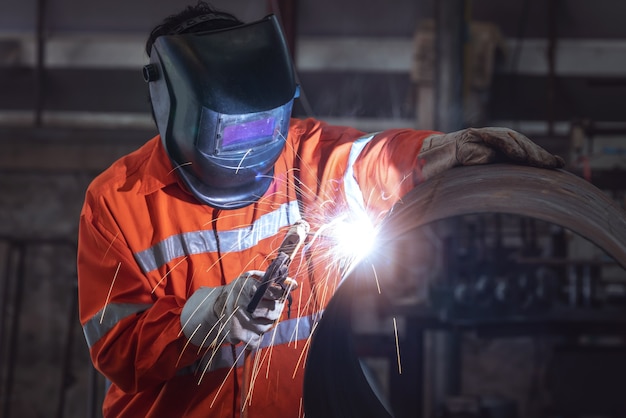 Industrial worker with protective mask welding metal pipe in a factory