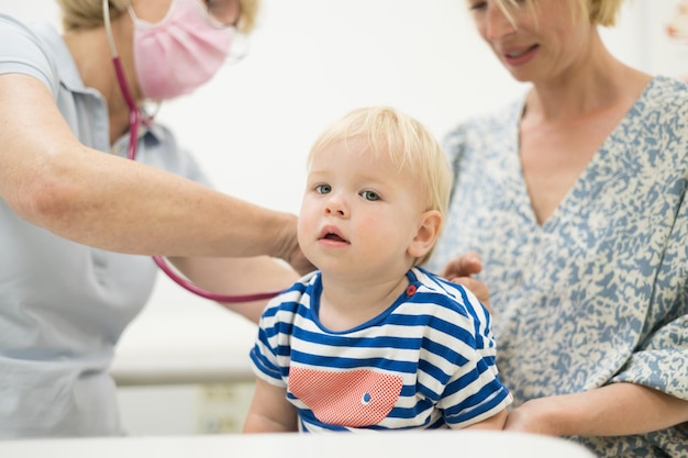 Photo infant baby boy child being examined by his pediatrician doctor during a standard medical checkup in