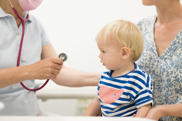 Photo infant baby boy child being examined by his pediatrician doctor during a standard medical checkup in