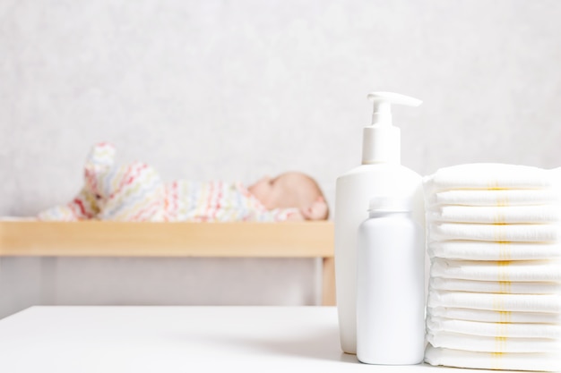 Infant baby care products. Lotion, powder and diapers on changing table in nursery. Baby cosmetics and hygiene concept.