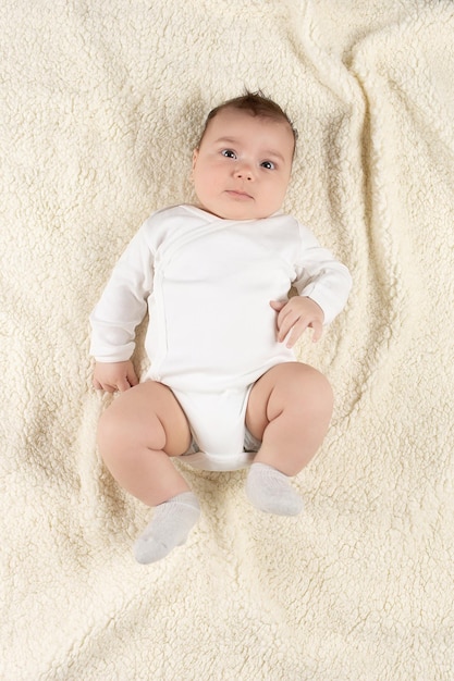 An infant in a white bodysuit lies on a soft blanket Mockup for advertising design celebration postcards