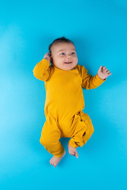 An infant in a yellow bodysuit lies on a blue background Funny little toddler Mockup for advertising design celebration postcards