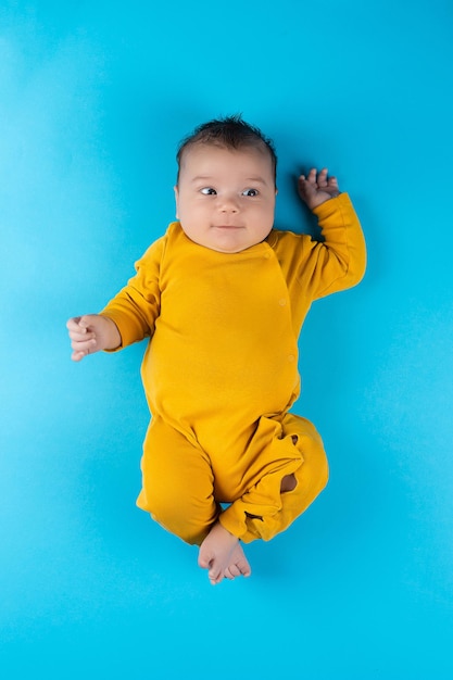 An infant in a yellow bodysuit lies on a blue background Funny little toddler Mockup for advertising design celebration postcards