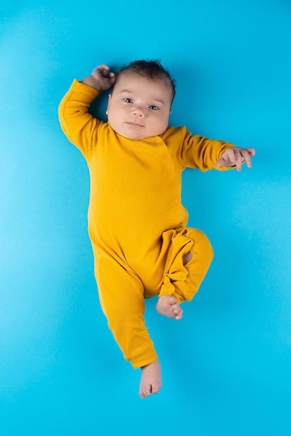 An infant in a yellow bodysuit lies on a blue background Funny little toddler Mockup for advertising design celebration postcards