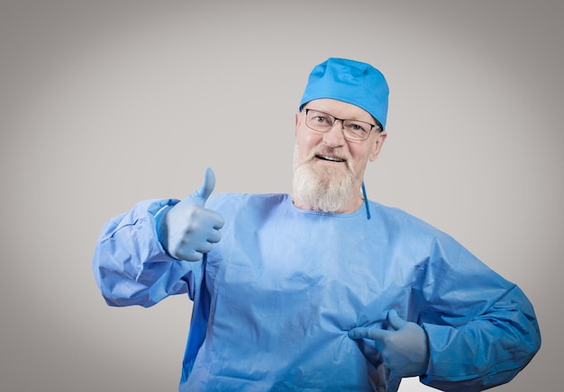 Infectious disease doctor with a gray beard in a blue protective overalls and rubber gloves shows a thumbs up