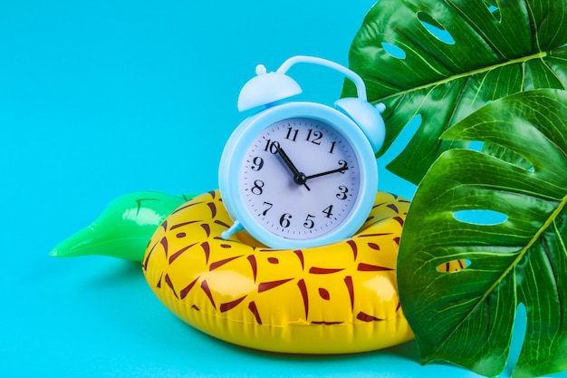 Inflatable pineapple on a blue background with clock and monstera leaves