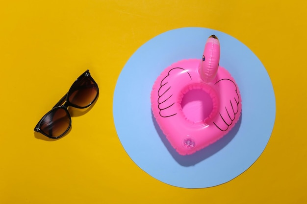 Inflatable pink flamingo and sunglasses on yellow background with pool. Summer vacation concept. Minimalism. Top view. Flat lay