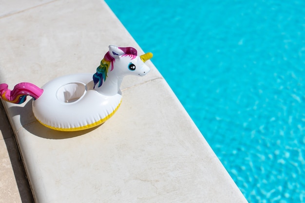 Inflatable pink mini rainbow unicorn, cocktail stand near swimming pool on bright sunny day, copy space.