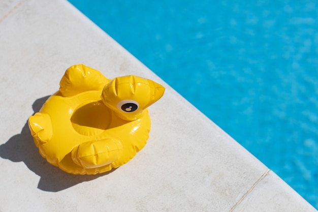 Inflatable yellow mini duck, cocktail stand near swimming pool on bright sunny day, copy space. Top view.