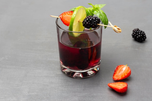 Infused summer drink with blackberries and green basil in glass Lime strawberry and blackberry on skewer