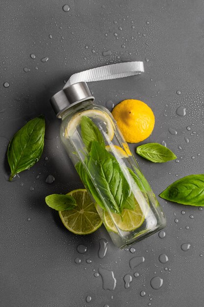 Photo infused water with lemon lime and basil in a transparent glass bottle on a gray background