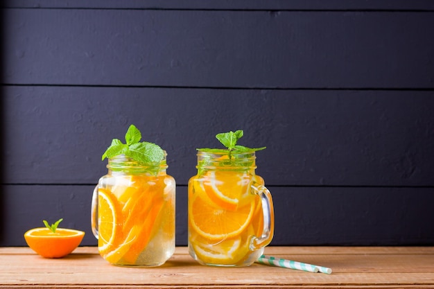 Infused water with orange fruit lemon and mint Iced summer drink in mason jar on wooden boards