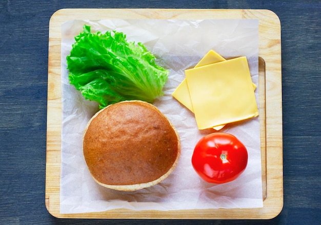 Photo ingredients for burger bun onion lettuce and pickled cucumber on wooden board