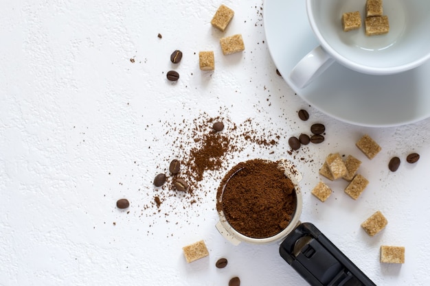 Ingredients for coffee: ground coffee in the horn of the coffee machine, sugar and a cup. Top view with copy space