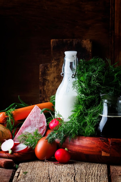 Ingredients for cold soup with vegetables herbs and meat products old wooden table selective focus.