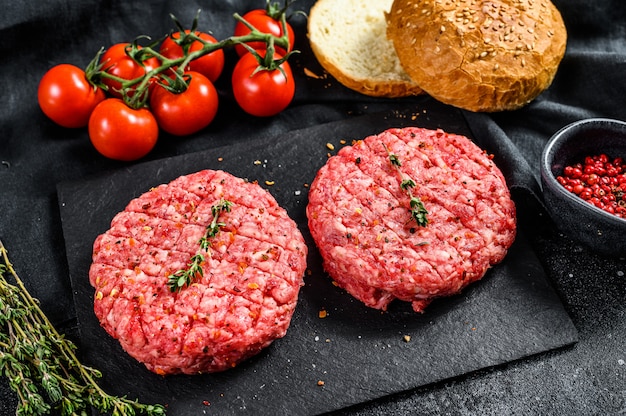 Ingredients for cooking burgers. Minced beef patties, buns, tomatoes, herbs and spices. Black surface. Top view