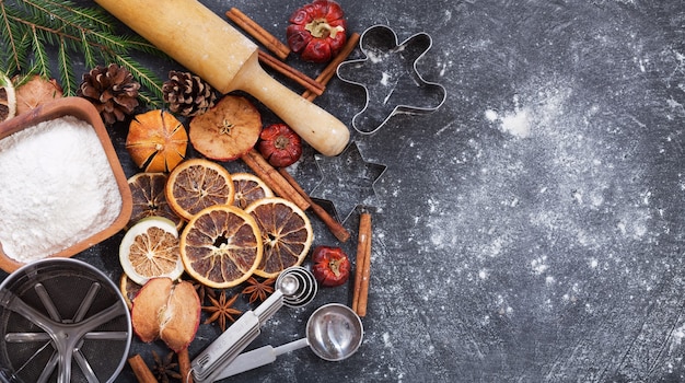 Ingredients for cooking Christmas baking: flour, kitchen utensils and dried fruits on dark background, top view