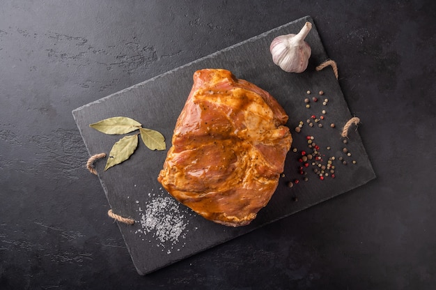 Ingredients for cooking homemade baked meat in marinade on a marble board on a dark background.