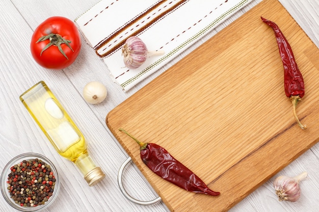 Ingredients for cooking meat or fish. Glass bowl with allspice peppers, bottle of oil, garlic, chili pepper, tomato and onion on a wooden cutting board. Top view.