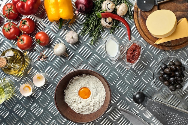 Ingredients and dough for making pizzas with an overhead view on freshly mixed mounds of pastry a jar of olive oil and pot of tomato sauce overhead view