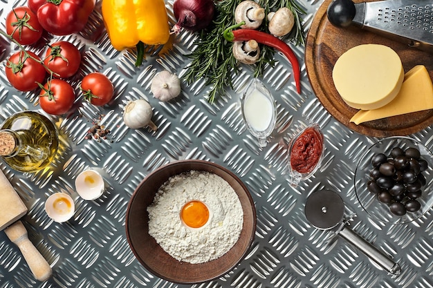 Ingredients and dough for making pizzas with an overhead view on freshly mixed mounds of pastry a jar of olive oil and pot of tomato sauce overhead view