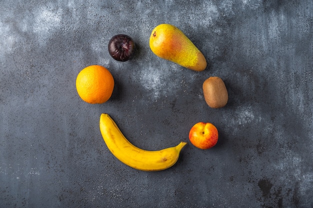 Ingredients for fruit salad lies in the shape of a circle on a dark wooden surface