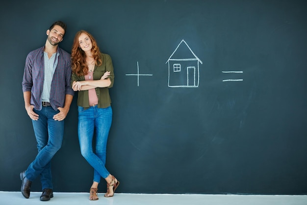 Ingredients for a happy life Shot of a young couple standing in front of a blackboard with symbols written on it