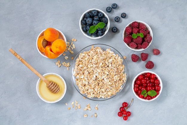 Ingredients for healthy breakfast. Oatmeal, honey with bowls of fresh summer fruits and berries: Apricot, Blueberry, Raspberry, Red Currant