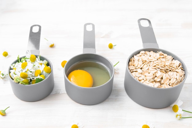 Ingredients for a homemade hair mask chamomile oatmeal and an egg on a wooden table