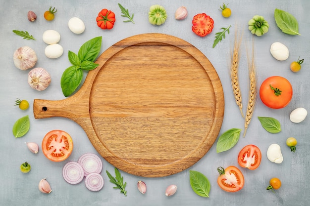 The ingredients for homemade pizza with wooden pizza tray set up on grey concrete background top view