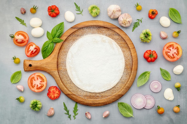 The ingredients for homemade pizza with wooden pizza tray set up on grey concrete background top view