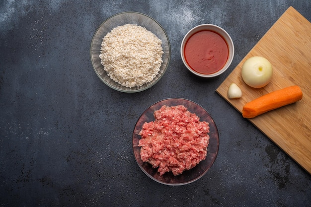 Ingredients for meatballs minced meat rice tomato paste onion garlic carrots on a cutting board on a