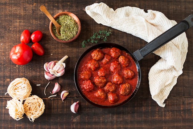 Photo ingredients and meatballs with tomato sauce on wooden background